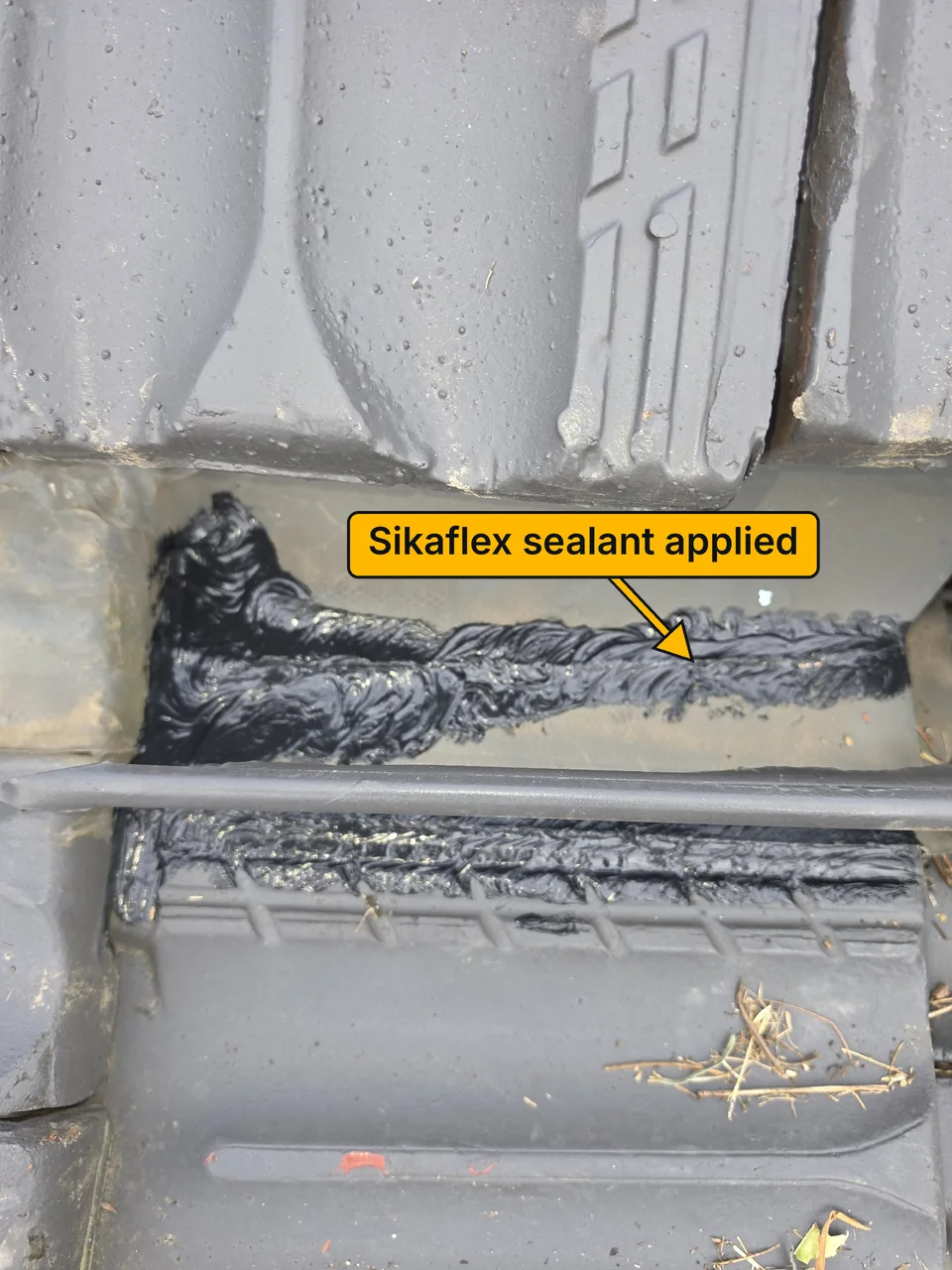 The repaired area after the work, with fresh black Sikaflex sealant applied on both sides of a raised bar. A label points to the sealant.
